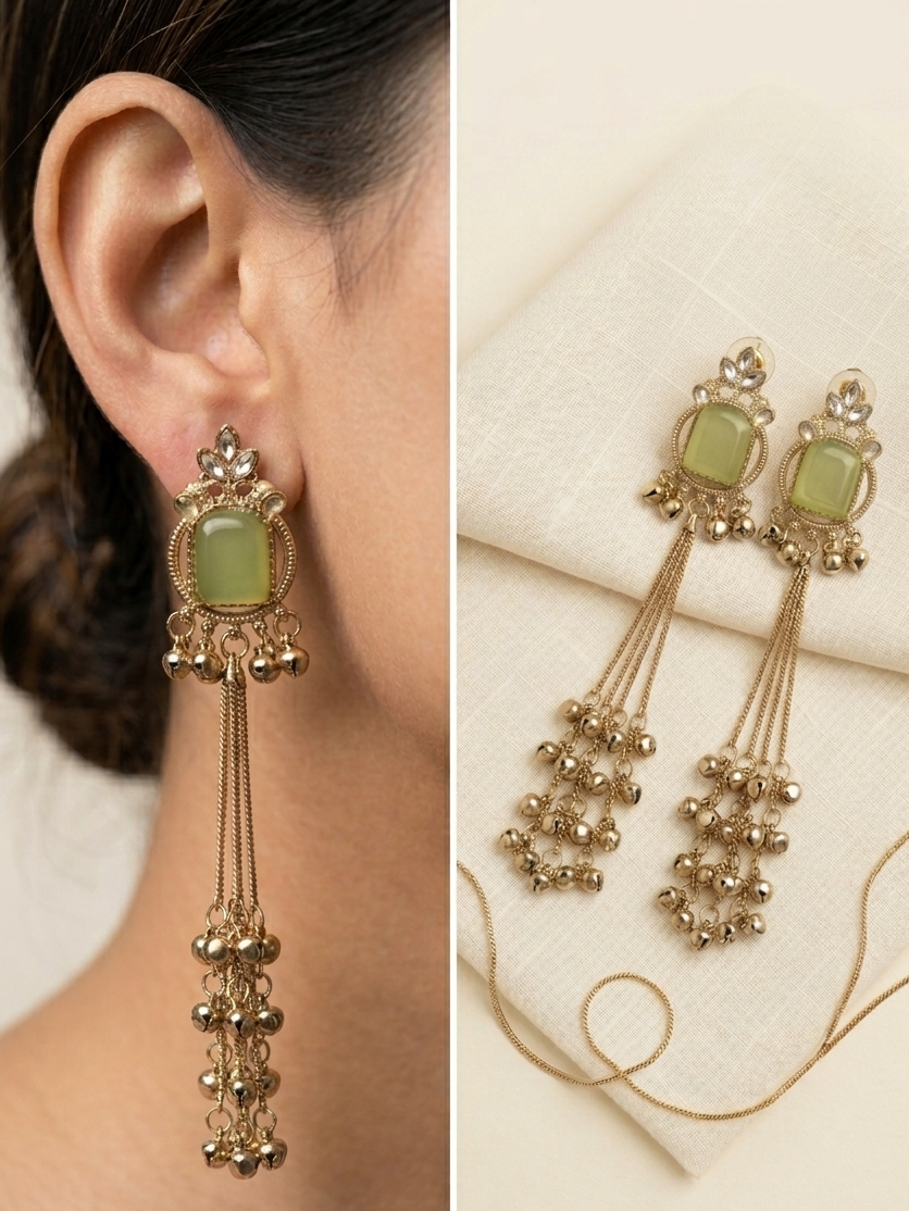 Gold earrings with green gemstones worn by a person, displayed on a white background.