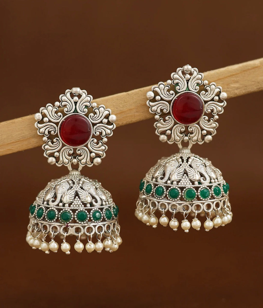 Ornate silver earrings with red and green stones on a brown background
